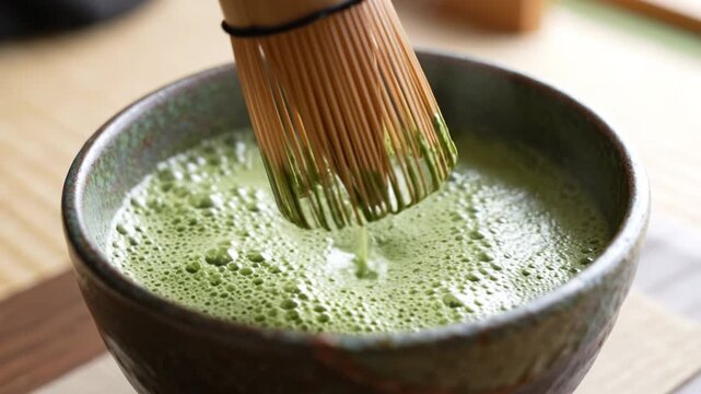 Green tea matcha froth in ceramic bowl with bamboo whisk showcasing traditional Japanese beverage preparation close up hand stirring vibrant frothy tea ritual natural organic drink