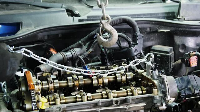Mechanics in gloves connects chain to lift engine with hoist in repair shop closeup. Technician uses hydraulic machine to remove motor at station