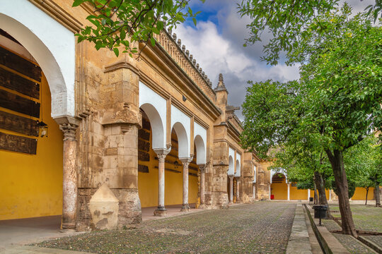 Enclosing walls of Mosque Cathedral of Cordoba, Spain, from the garden. Ancient stone masonry, green trees, cloudy sky