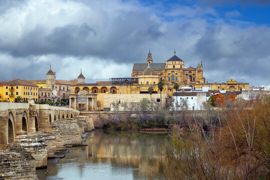 View of Mosque Cathedral from Roman Bridge in Cordoba, Spain. Historic city skyline over Guadalquivir river, cloudy sky