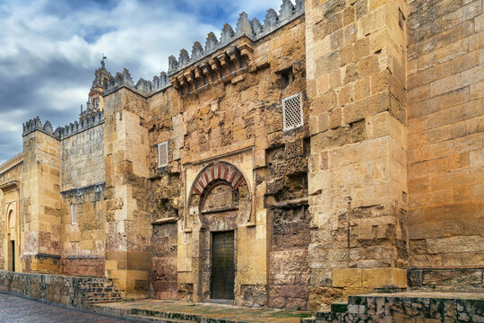 Exterior walls of Mosque Cathedral of Cordoba, Spain. Ancient stone facade with closed entrance, cloudy sky, no people