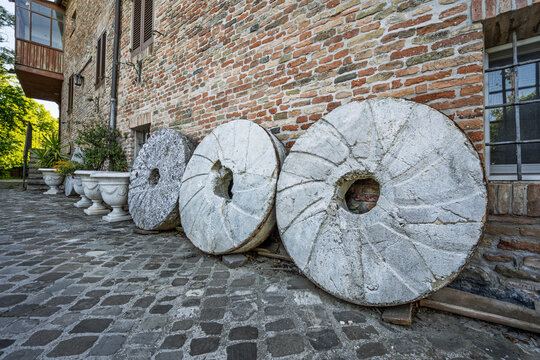 Old stone millstones displayed against a rustic wall in the village of Mondaino, Emilia‑Romagna, Italy