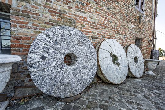 Old stone millstones displayed against a rustic wall in the village of Mondaino, Emilia‑Romagna, Italy