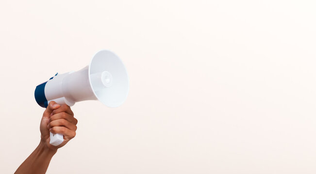 Hand holding white megaphone against white background with copy space for marketing announcements, social media alerts, and business promotions.