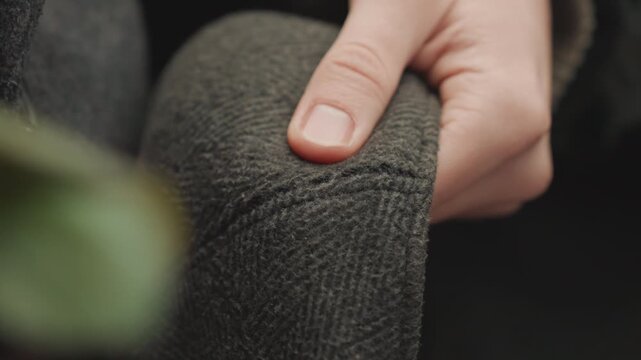 Closeup caucasian hands inspecting wool cap, textured tweed fabric and top button in frame, gentle pressing of seam, close tactile quality check by creator in cozy studio, soft natural light, muted