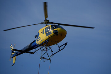 Fototapeta premium blue and yellow helicopter flying in a clear blue sky carrying equipment