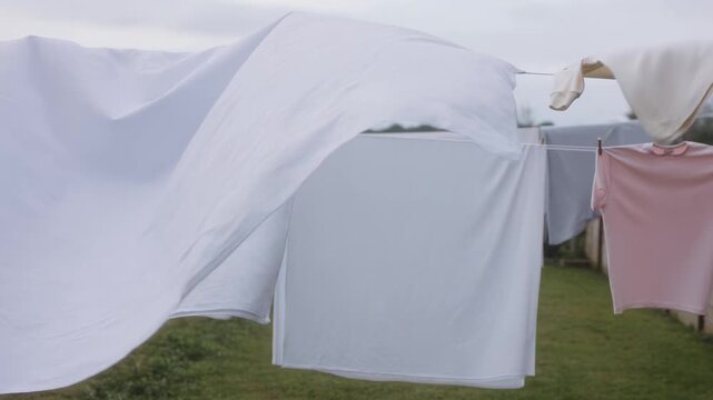 White laundry blowing in the wind on an outdoor clothesline. Fresh sheets and clothes drying in a backyard. Domestic chores and household concept