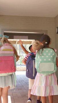 Three students raising hands then stepping through passage backpacks adjusting heading schoolyard