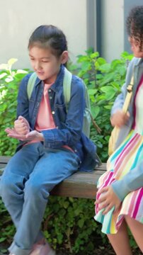 Curly-haired girl approaching and waving, school girl leading clapping game, boy mirroring on bench