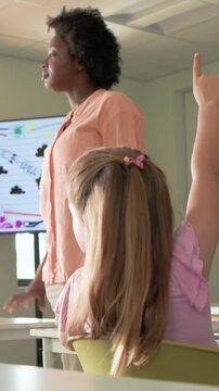 Vertical video: Responding teacher in peach top moving to raised hand pupil in class, touching hair