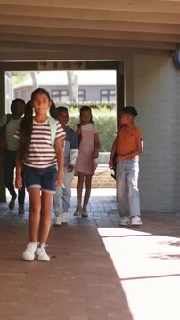Vertical video: Leaving doorway lead girl walking toward class on campus walkway with backpacks