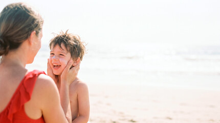 Fototapeta premium Mother applying sunscreen to her happy child's face at the beach