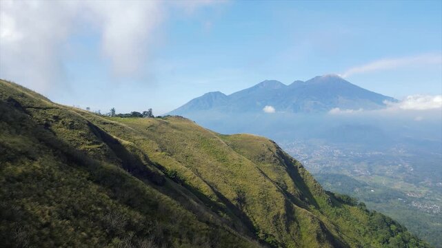 Cinematic 4K view of Mount Arjuno Welirang from high grassy slopes on a clear sunny day.