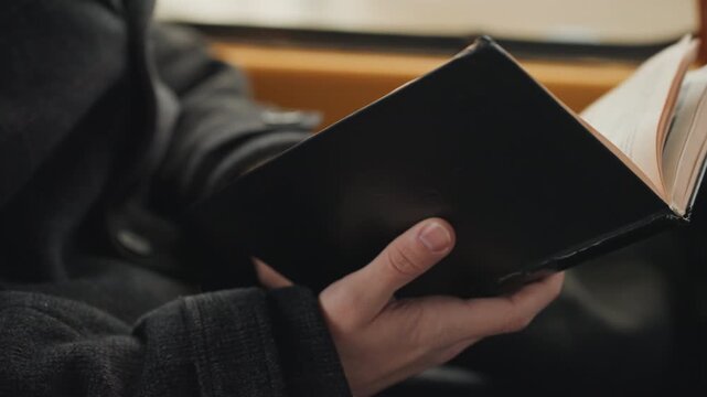 Hands holding journal on train, creator reading quietly in cozy sweater, leatherbound pages turning by window light, focused hands and slow commute atmosphere, reflective mood and subtle inspiration