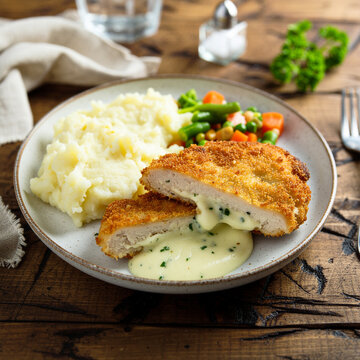 A plated Chicken Kiev on a rustic table, golden crispy breaded chicken breast sliced open revealing molten garlic herb butter filling