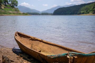 Obraz premium A weathered wooden boat rests on the calm lakeshore beneath a bright blue sky.