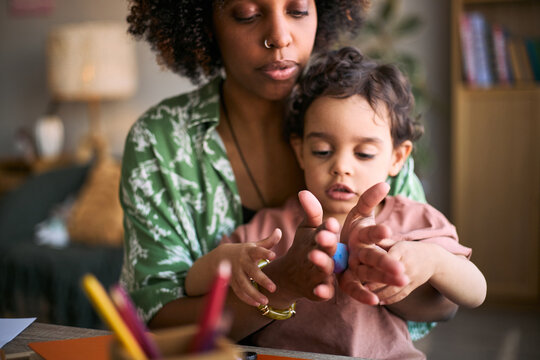 Black mother guiding toddler shaping modeling clay at home, supporting sensory play and early learning