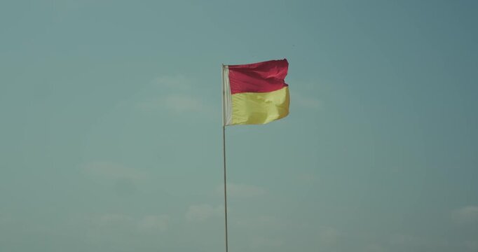 Red and yellow safety flag on pole against clear sky beach warning and lifeguard signal concept
