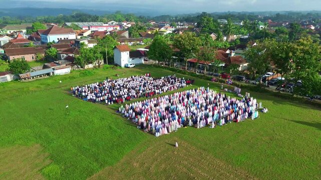 Drone view of Eid prayer gathering, hundreds of Muslims praying together on a wide grassy field.