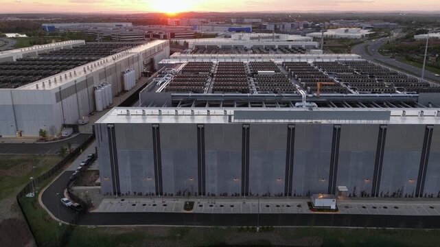 Large data center campus in Ashburn, Virginia, USA at sunset showing expansive server buildings, rooftop cooling systems and modern cloud infrastructure near Washington DC. Aerial lateral shot.