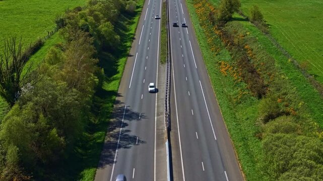 Four-lane highway cutting through green rural landscape in France. Aerial backward