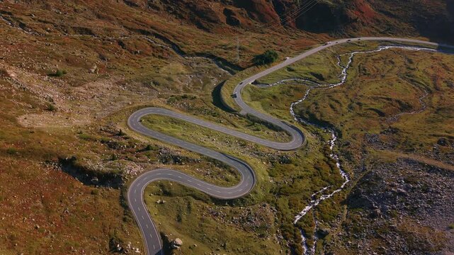 Aerial shot of the winding Julier Pass road cutting through rugged Swiss Alps with autumn colors.
