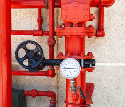 Red Industrial Fire Sprinkler System with Pipes and Gauges Against a Wall