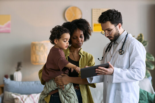 African American mother holding child while doctor showing tablet during home visit, discussing pediatric care and treatment