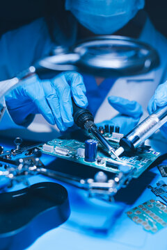 Hands in white gloves carefully repair a broken mobile device, meticulously working on the intricate internal electronics and circuit board