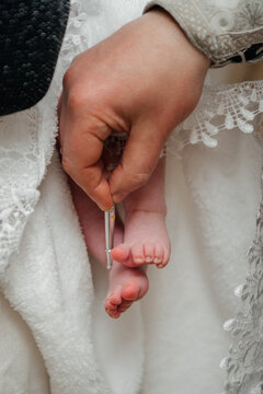 A significant moment of the Orthodox baptism ritual where a priest uses a special brush to anoint a baby's foot with holy chrism (myrrh). The baby is wrapped in a traditional white lace cloth. 