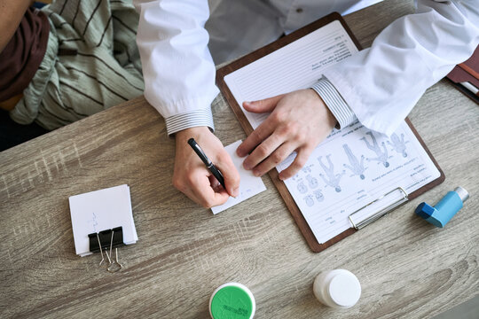Overhead shot of doctor writing prescription beside patient chart and inhaler during consultation