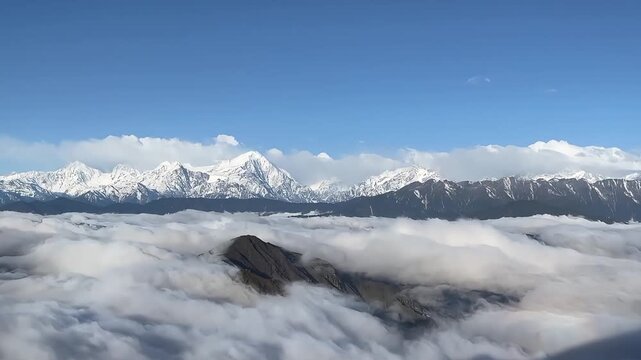 Stunning 4K timelapse of a thick sea of clouds rolling over jagged snow-capped mountain peaks in the Hengduan Mountains of China during a bright day.