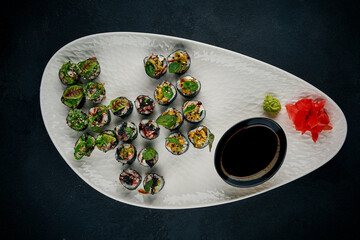 Large sushi set with assorted rolls topped with avocado, seaweed salad, and caviar, served on a white platter with soy sauce, ginger, and wasabi © ismishko