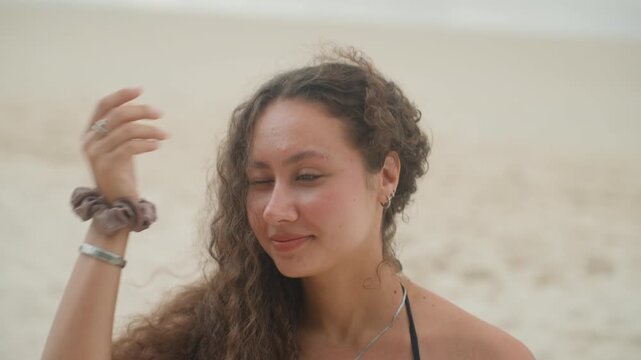 Multiracial woman on island shore close portrait, soft sunkissed skin and downcast gaze, slight smile, loose curls and necklace detail, introspective mood, studentartist and memory keeper roles,