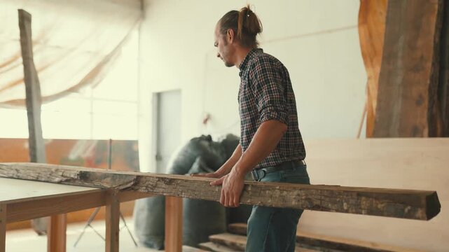 Carpenter lifting heavy wood beam in workshop