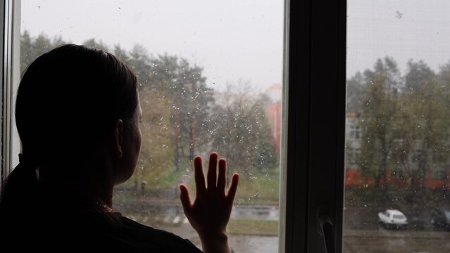 Sad woman looking through a rainy window. A lonely young woman looks out the window in depression