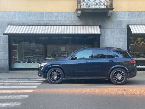 Mercedes Benz GLE SUV parked on city street next to storefront with striped awning, luxury lifestyle