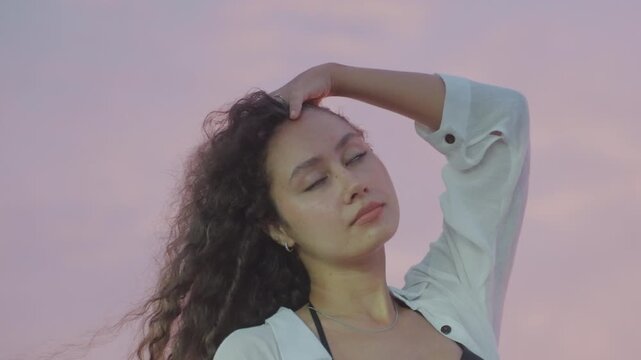 Peaceful evening woman. Calm female figure at sunset. Serene woman standing beside water during evening twilight sky. Tranquil lady with flowing hair enjoys peaceful sunset by riverbank