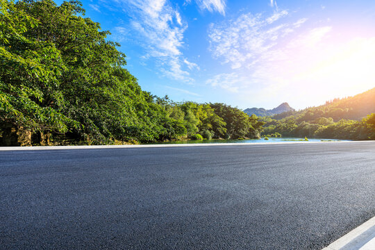 Empty asphalt road through green mountain forest under clear blue sky