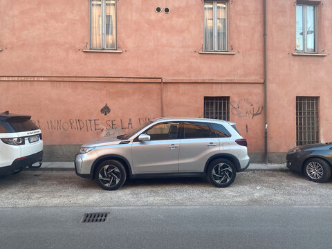 Suzuki Vitara, Land Rover Discovery, and other cars parked along an old terracotta building wall with handwritten graffiti