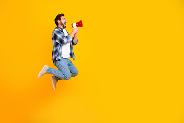 Obraz premium Young man jumping and shouting into a megaphone on a vibrant yellow background expressing excitement and making an announcement