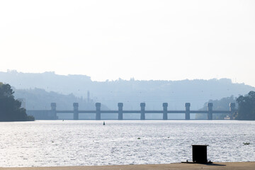 Fototapeta premium Dam structure across river with hazy hills and soft atmospheric light in Portugal, Portugal, Lixa, 17 October 2025