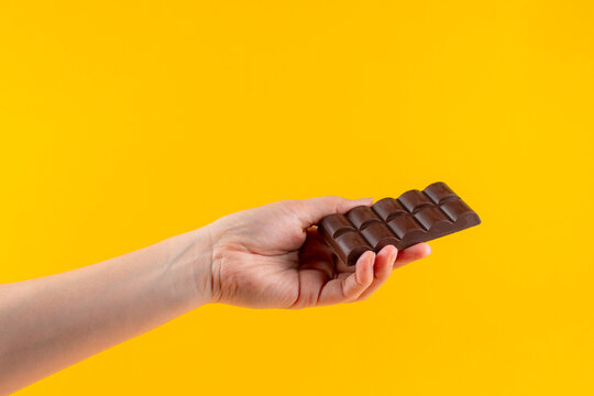 A large chocolate bar in hand, against a yellow background.