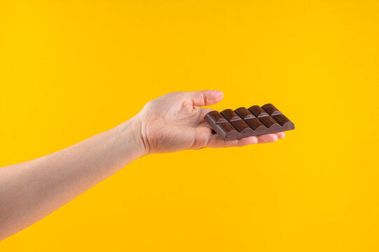 A large chocolate bar in hand, against a yellow background.