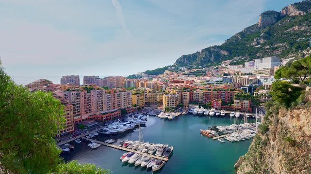Panning shot over Fontvieille port in Monaco with marina, luxury yachts, colorful residential buildings, and rocky coastline, showcasing Mediterranean lifestyle and upscale waterfront living.