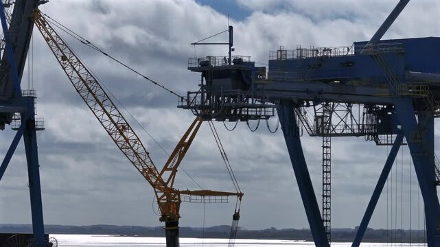 Close-up shot of port cranes with luffing jib and ship-to-shore structure against overcast sky beside open waterway