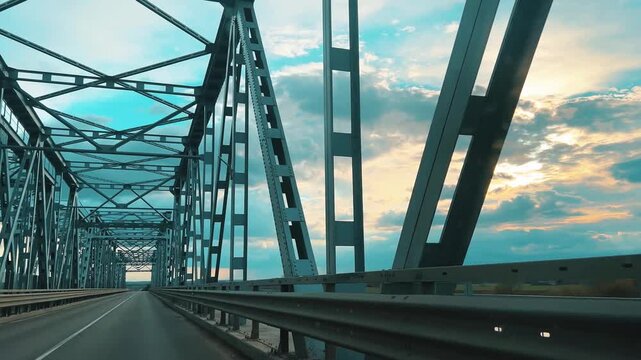 Low-angle vehicle perspective crossing a steel bridge structure during golden hour. Suitable for engineering, logistics, automotive marketing, and travel industry content.
