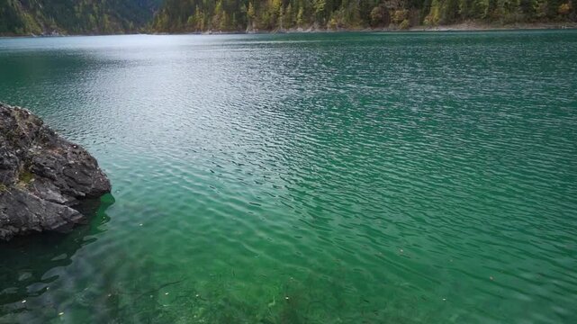 A view of Long Lake (Chang Hai), the highest and largest lake in Jiuzhaigou National Park. The shot features deep turquoise waters and a rocky foreground, looking down massive V-shaped glacial valley.