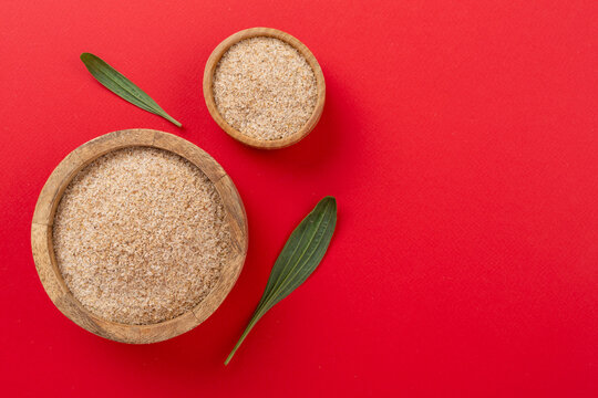 Psyllium husk powder with fresh leaves on color background, top view