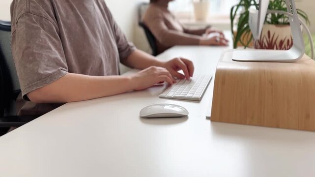 This video clip captures a close-up view of hands typing on a keyboard in a contemporary office setting. The relaxed atmosphere and clean workspace enhance productivity vibes, ideal for business or te